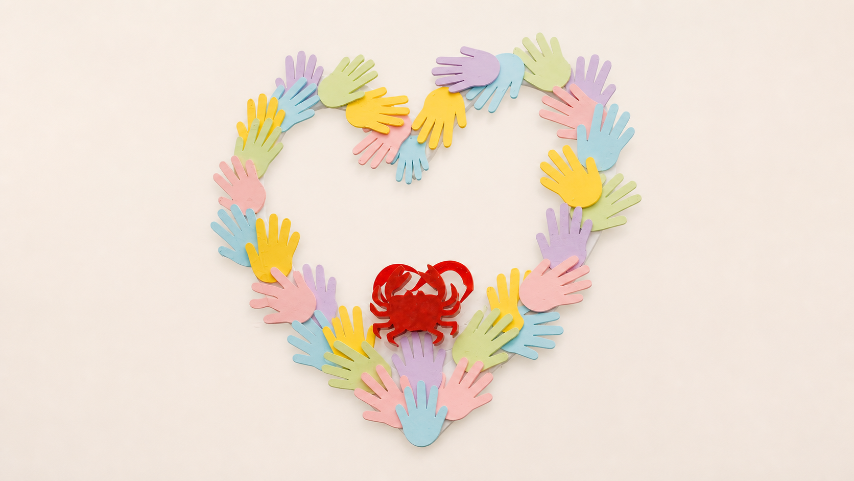 A heart outlined with colourful paper handprints around a small red crab, the PWF symbol