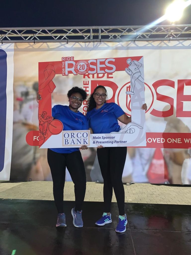 Two PWF volunteers holding the Ride for the Roses photo frame in the evening