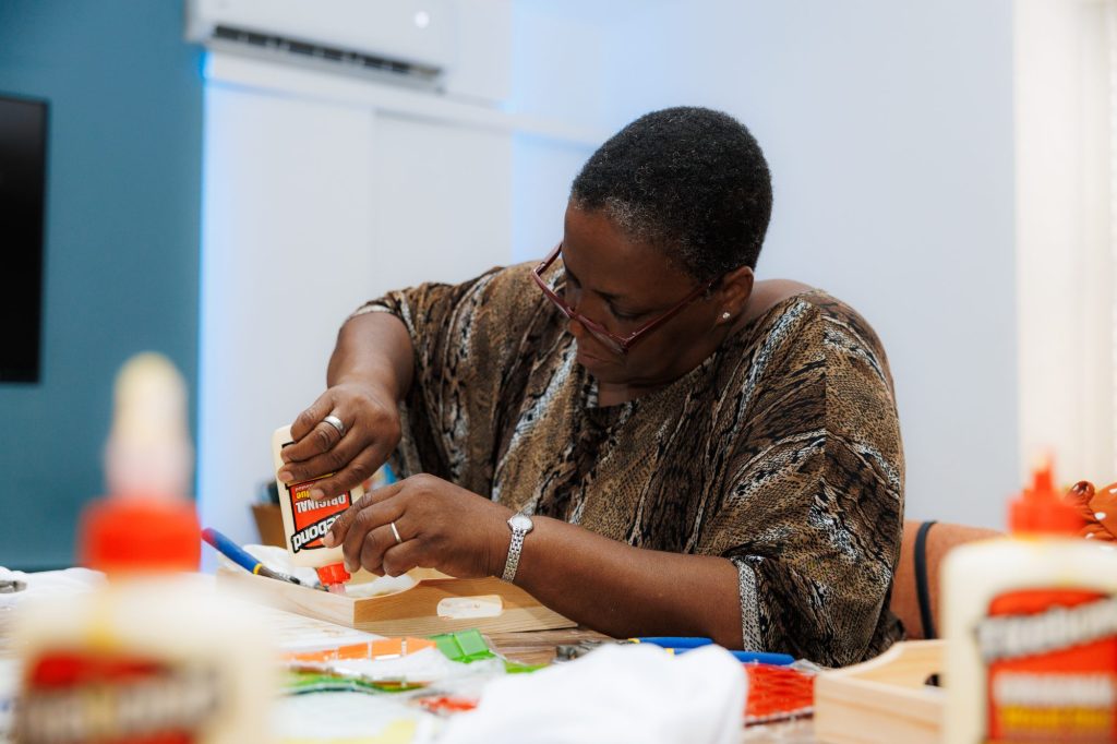 A participant applying glue to a wooden tray during a PWF mosaic workshop